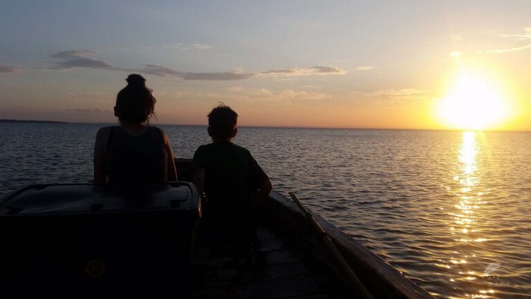 Zachód słońca na morzu, dwoje dzieci siedzi w łódce i podziwia zachód słońca.