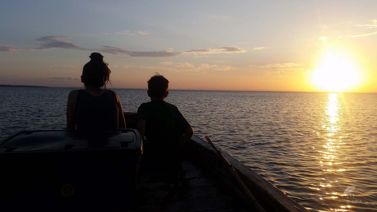 Zachód słońca na morzu, dwoje dzieci siedzi w łódce i podziwia zachód słońca.