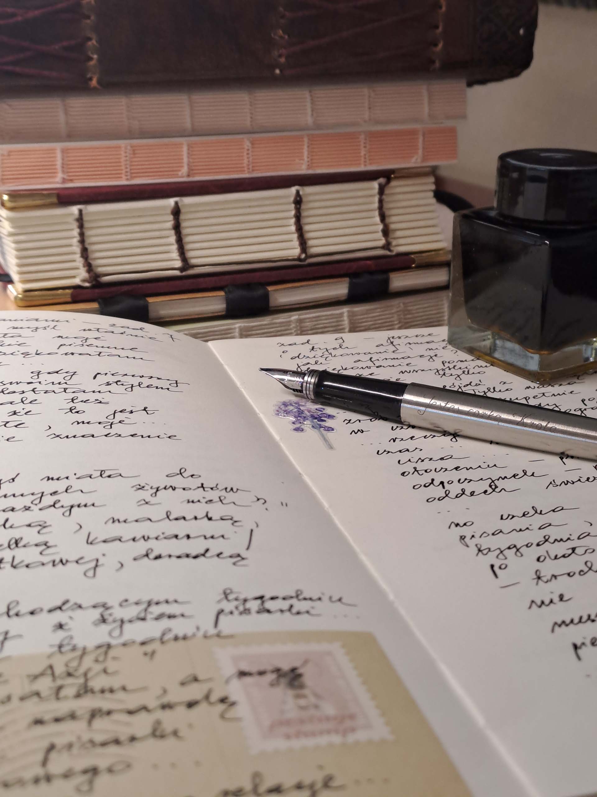 Otwarty zeszyt z zapiskami, na zeszycie leży otwarte, wieczne pióro i kałamarz z atramentem.