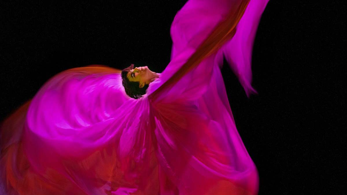 Tancerz na scenie w wirującym tańcu, w różowym stroju przypominającym skrzydła motyla.